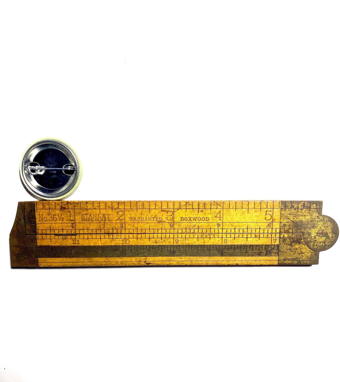 Wooden ruler with measurement markings on a white background measuring a pin back button.