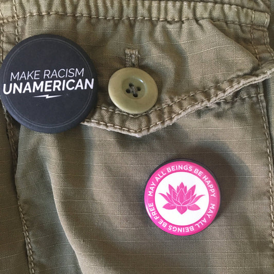 Two buttons on a jacket with one reading 'Make Racism Unamerican' and the other with a pink lotus design, may all beings be happy may all beings be free