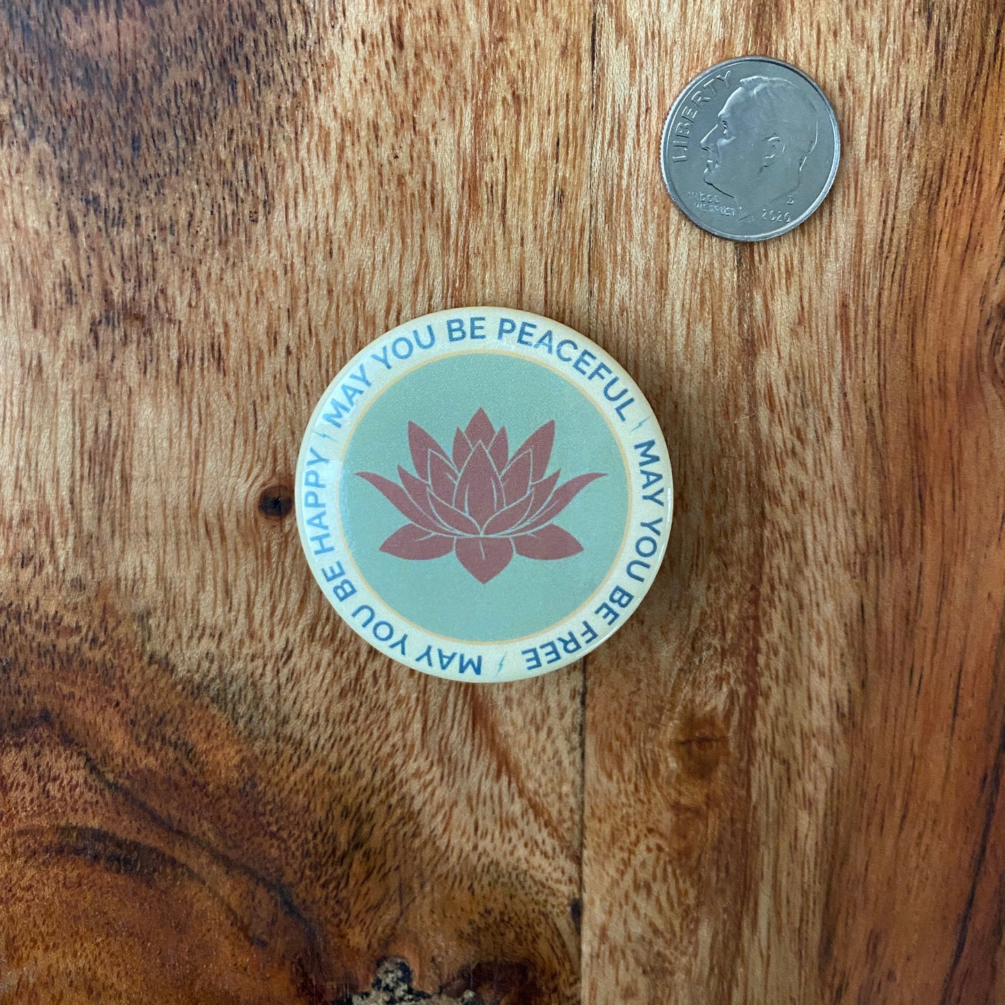 Round button with lotus flower design and text on a wooden surface with a coin for scale.