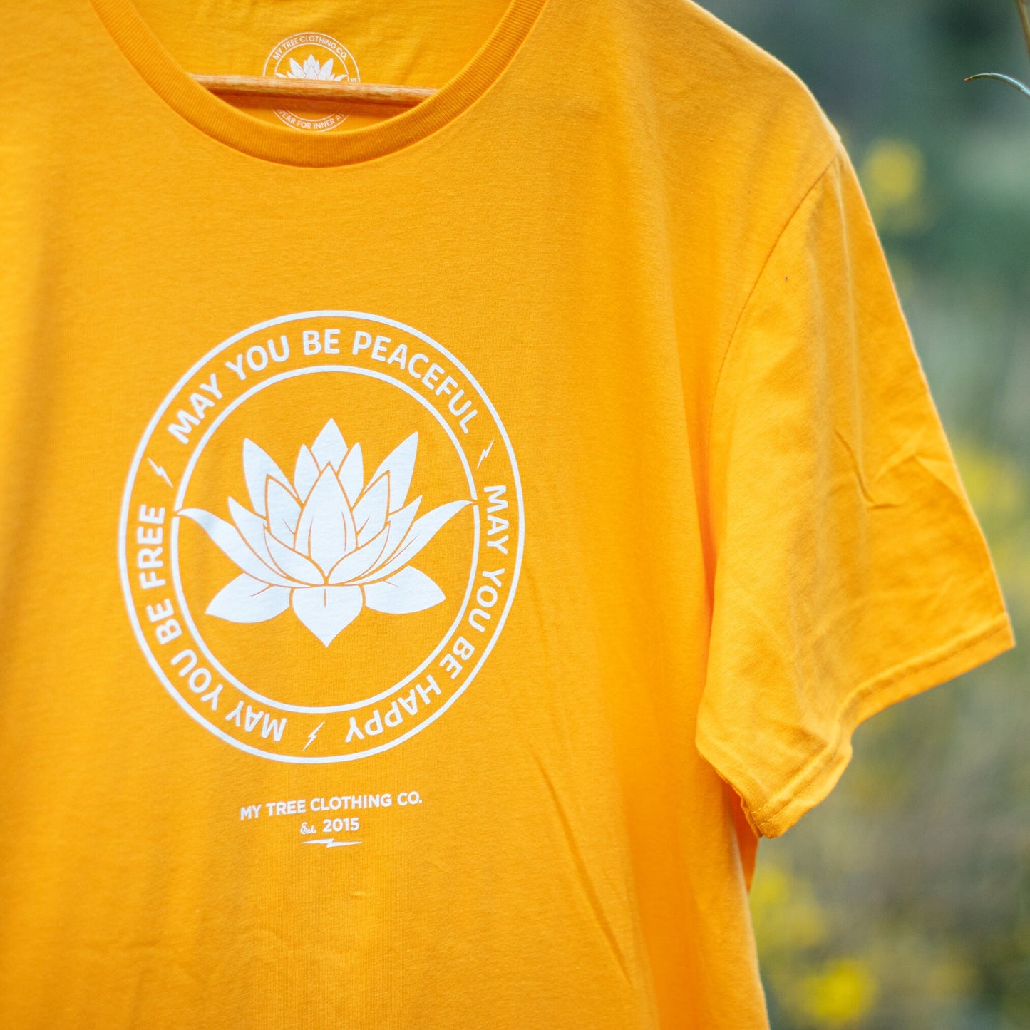 Yellow t-shirt with a white lotus flower graphic, may you be peaceful may you be happy may you be free.