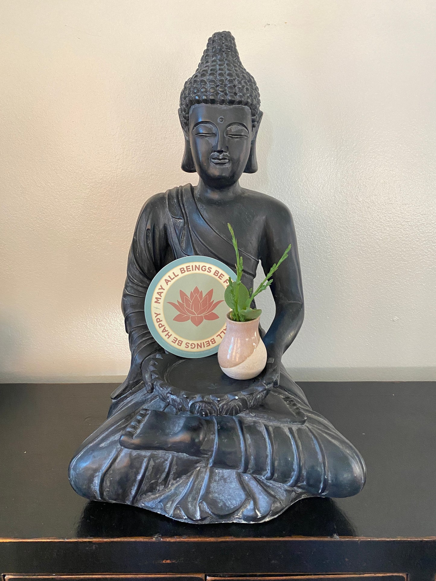 Buddha statue holding a 4" circle lotus flower design and text, MAY ALL BEINGS BE FREE MAY ALL BEINGS BE HAPPY.
