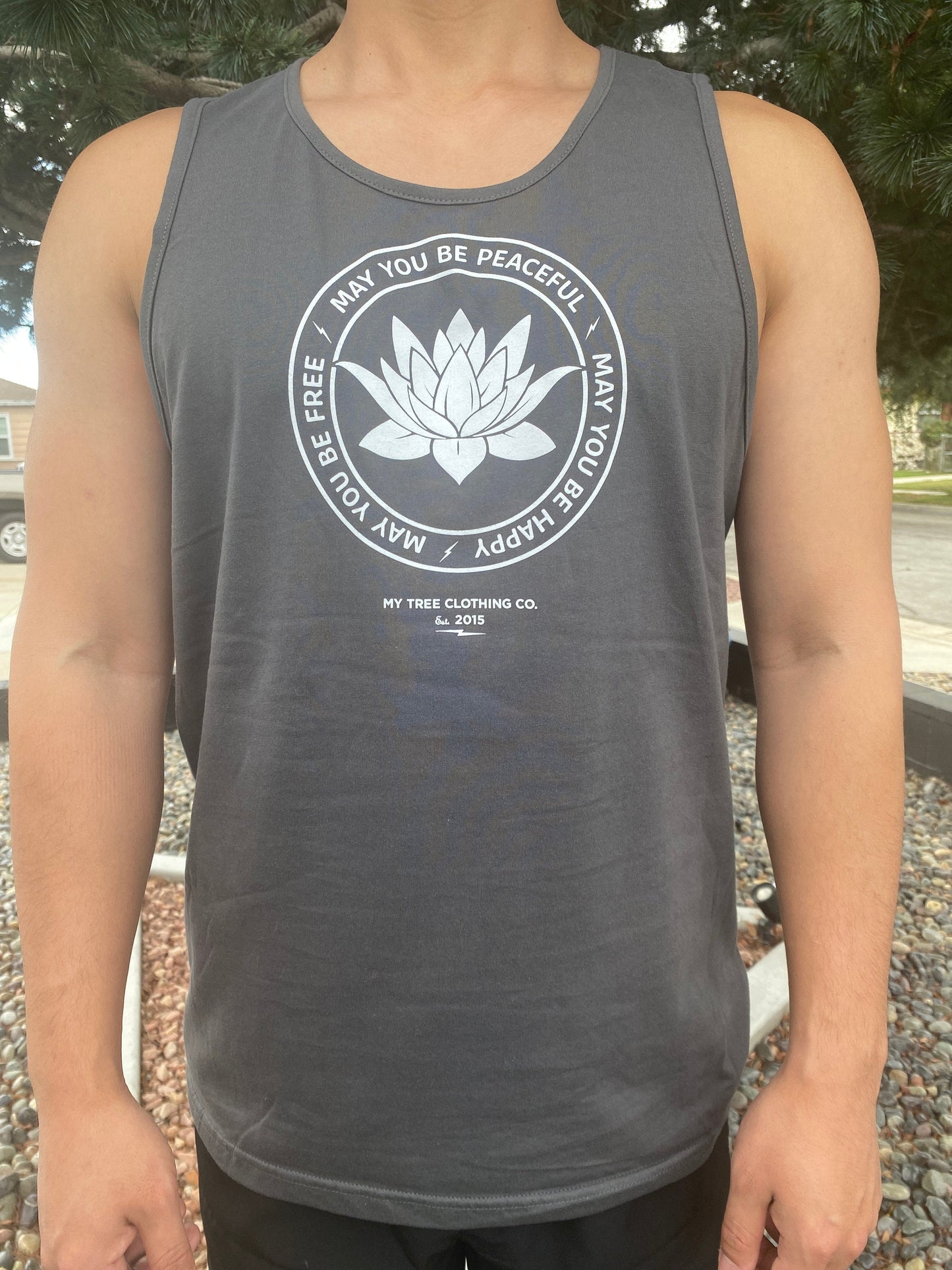 Person wearing a gray tank top with a lotus and the text, MAY YOU BE PEACEFUL MAY YOU BE HAPPY MAY YOU BE FREE.