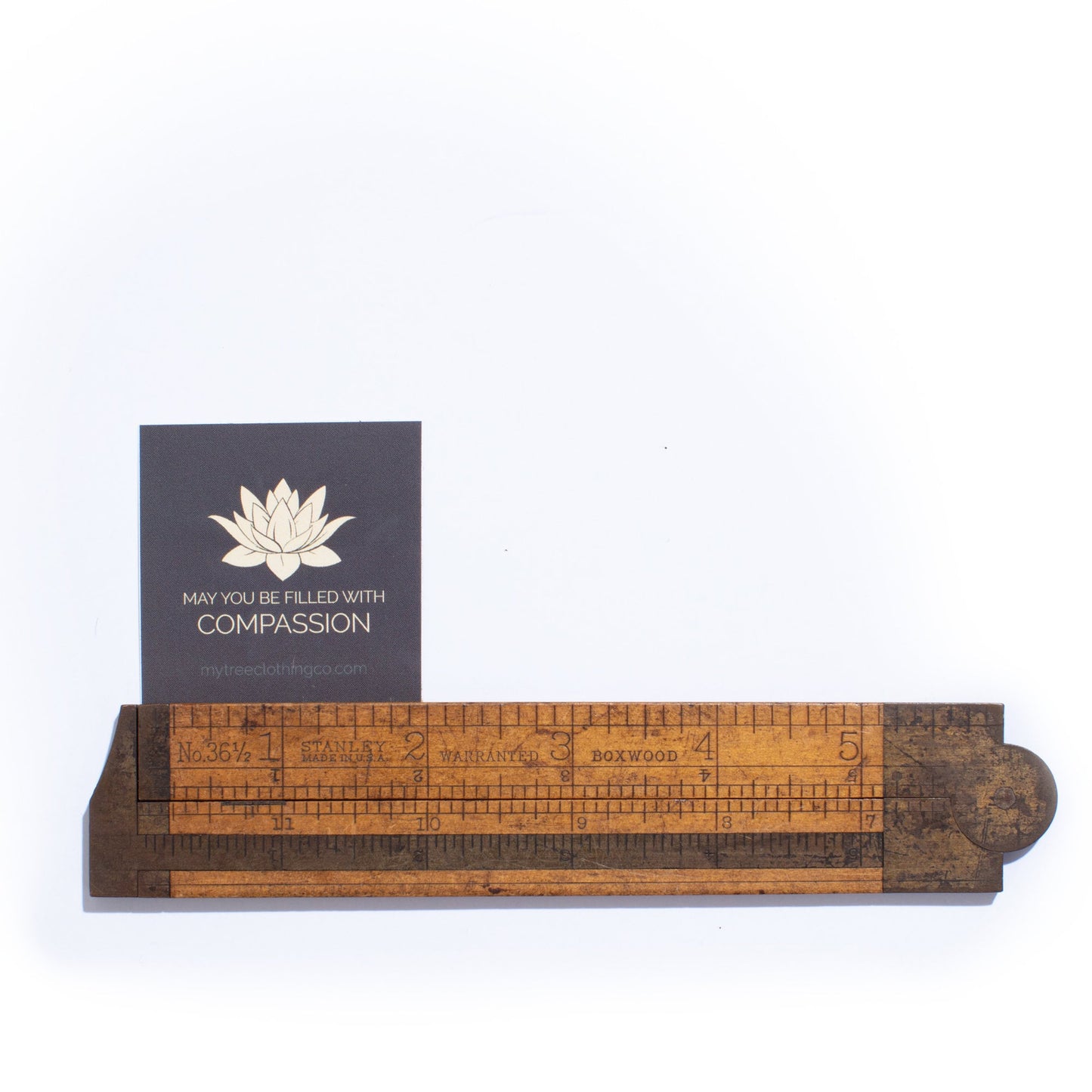 Wooden ruler with a 2" square lotus flower sticker with text 'May you be filled with compassion.'