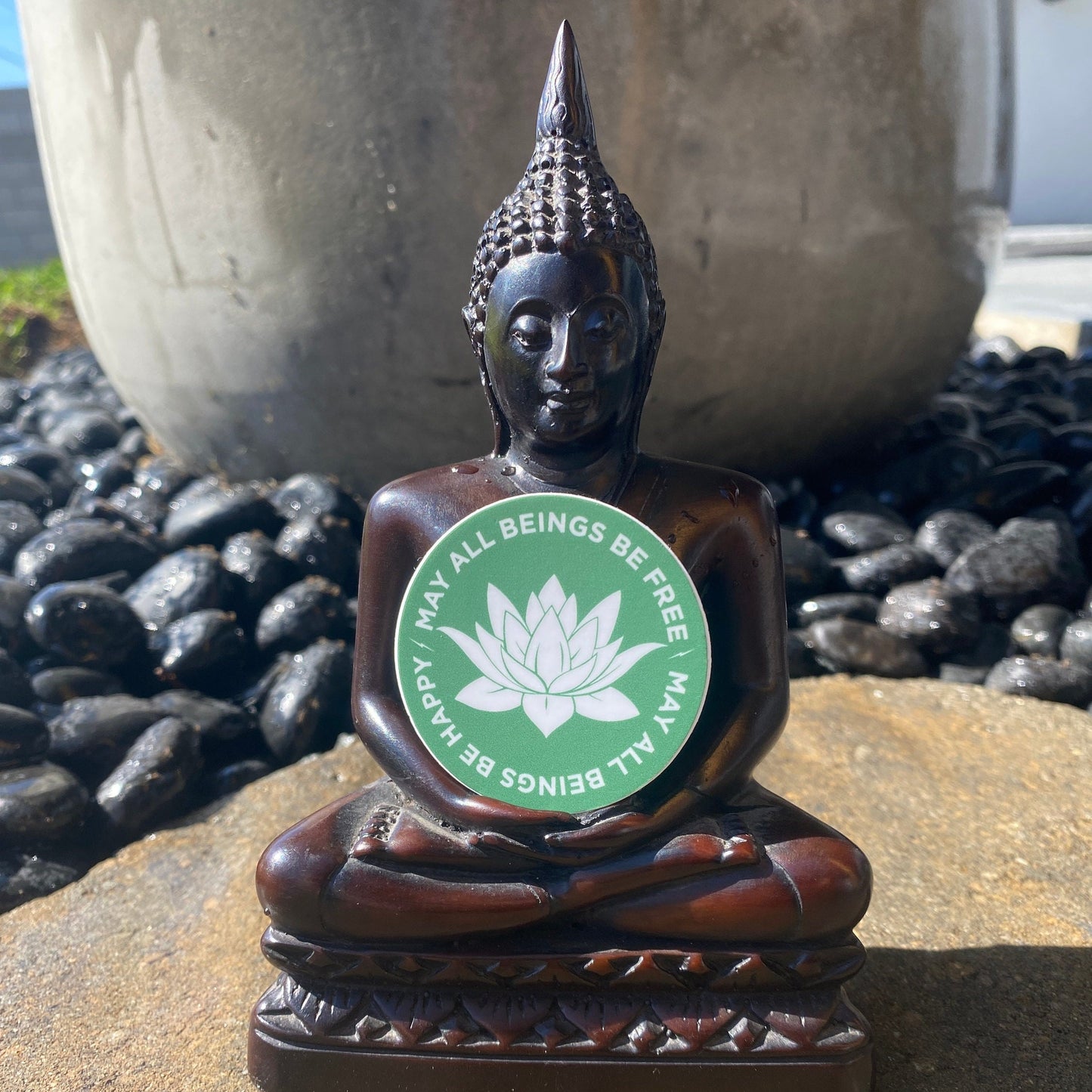Buddha statue with a 2" round green sticker with a white lotus Buddhist design and the text, may all beings be free may all beings be happy.