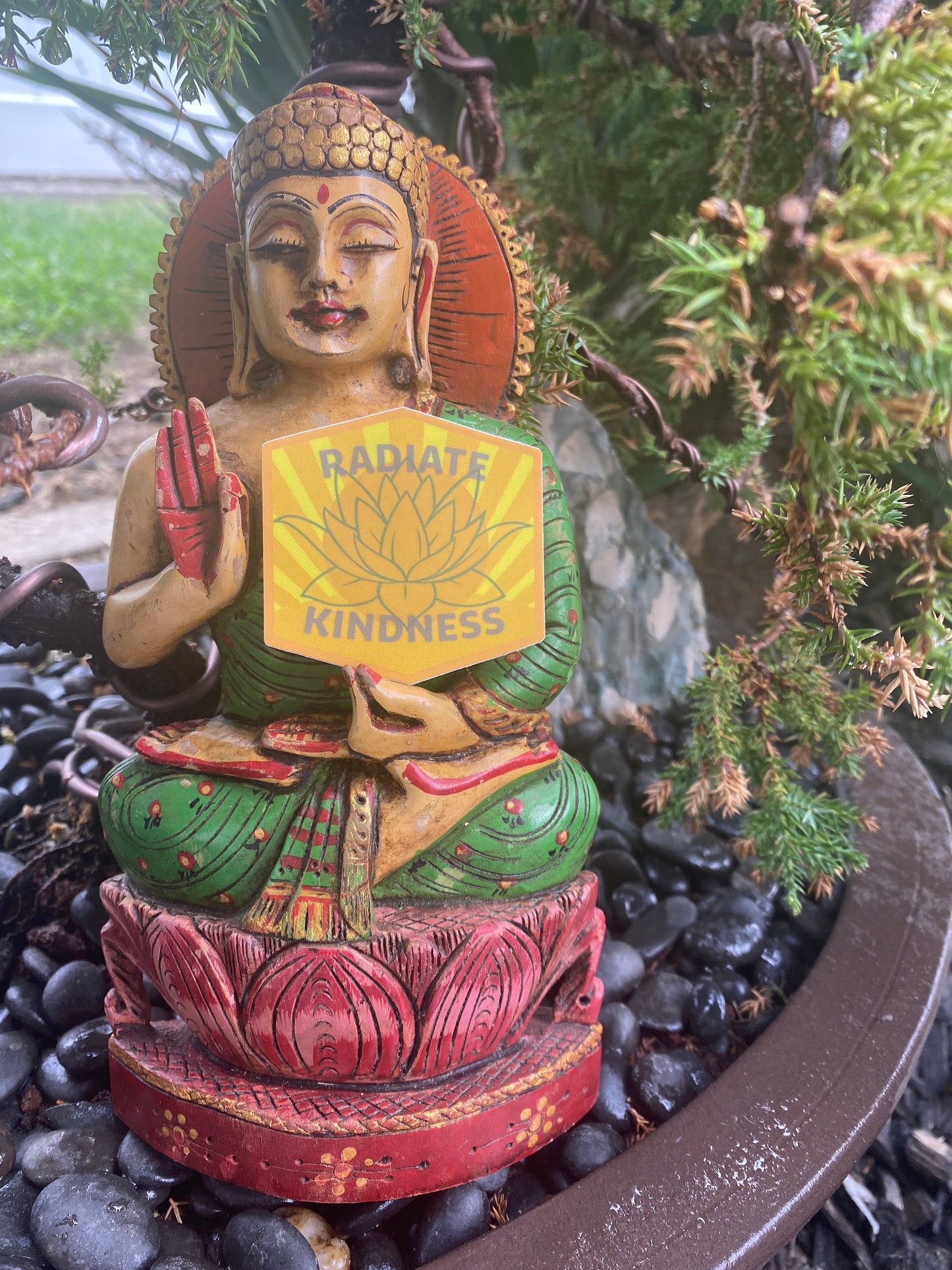 Buddha statue holding a sign with 'Radiate Kindness' in a garden setting