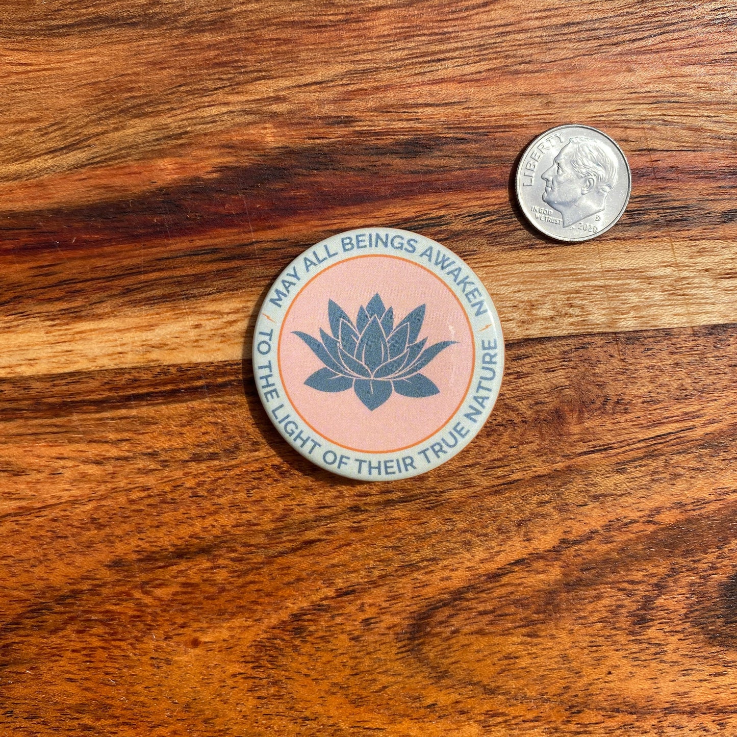 Round button with lotus flower design and text on a wooden surface with a coin for scale.