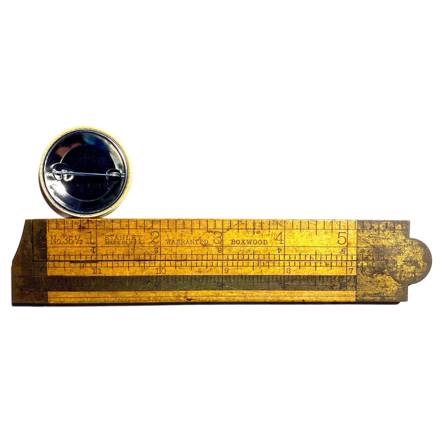 Wooden ruler with a round black and gold badge on a white background