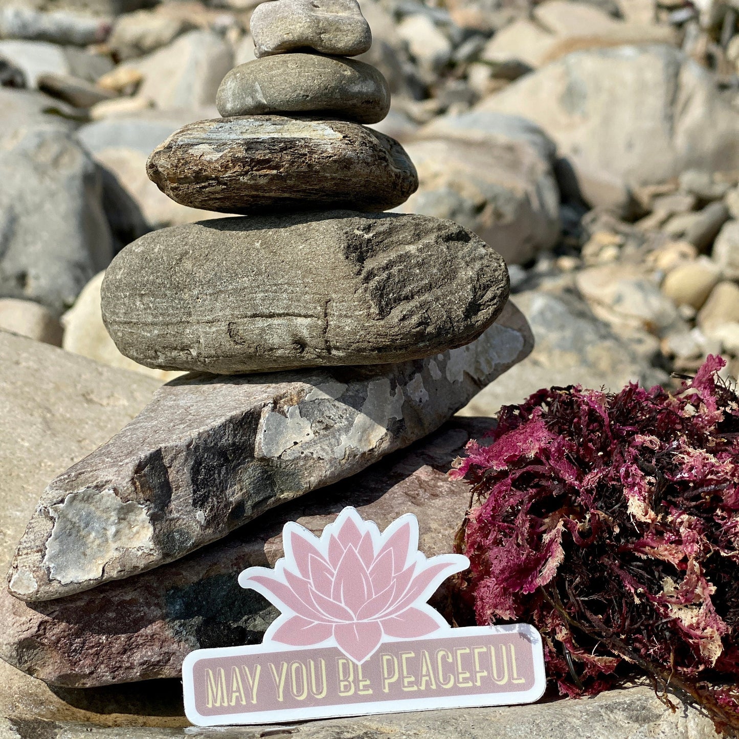 Stack of stones with a pink lotus flower with the text, may you be peaceful.