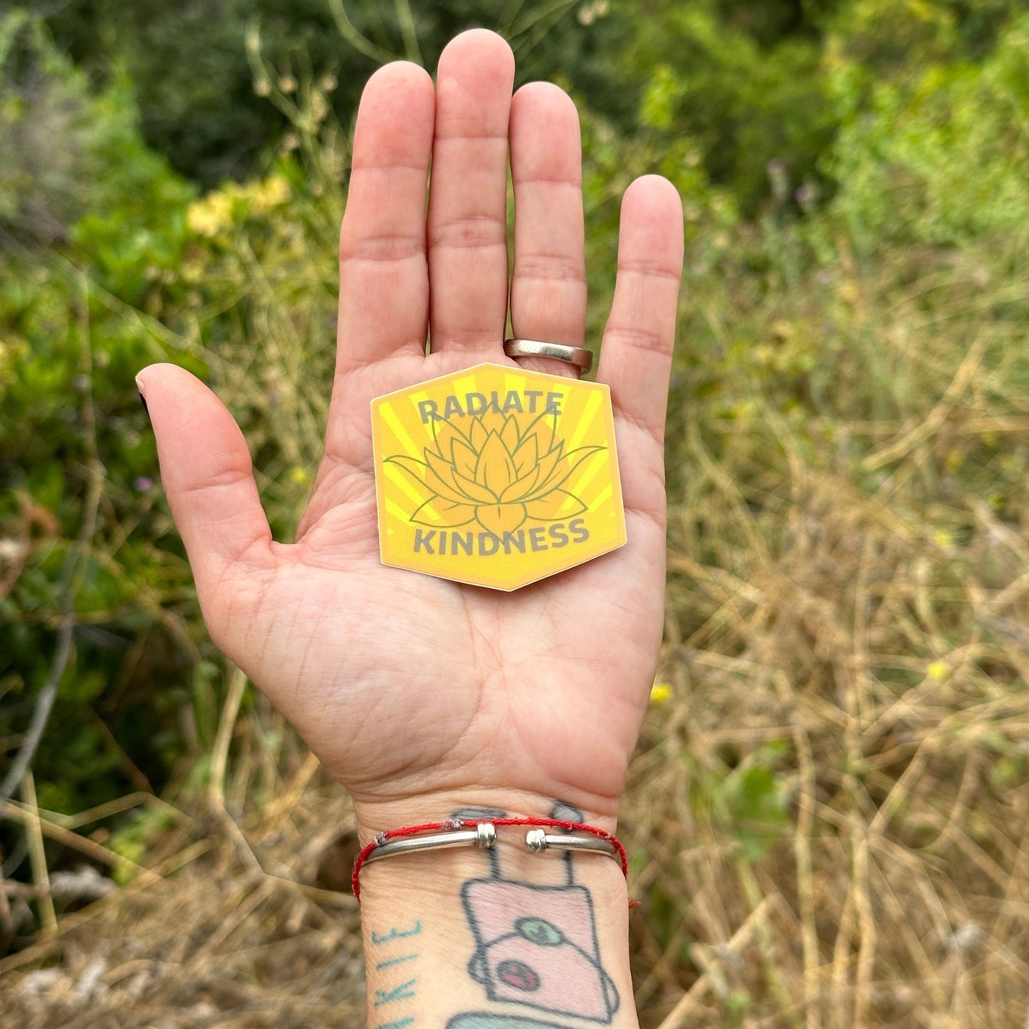 Hand holding a yellow 'Radiate Kindness' patch with a natural background