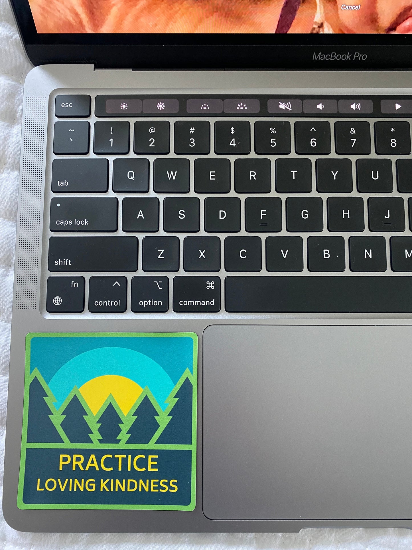 Laptop with a 'Practice Loving Kindness' sticker on a soft surface