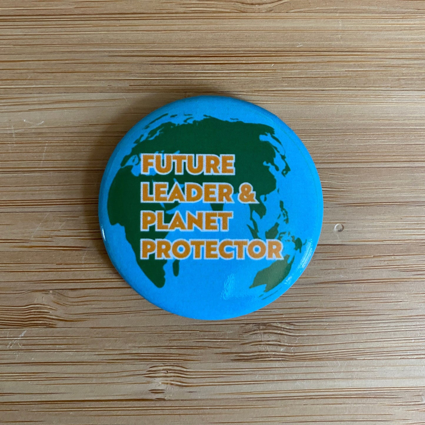 Button badge with 'Future Leader & Planet Protector' text on a world map design, placed on a wooden surface.