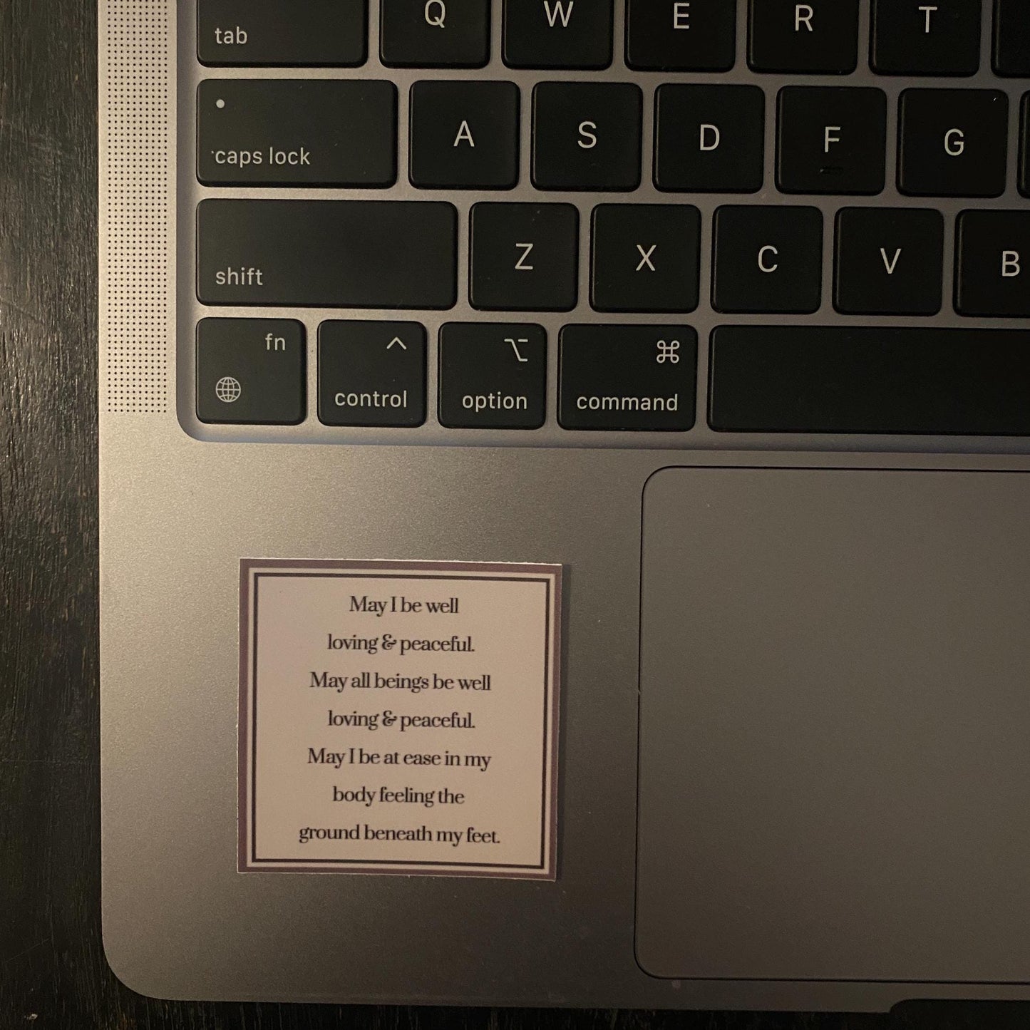 Laptop keyboard with a small 2" square Buddhist prayer the palm rest area containing text.