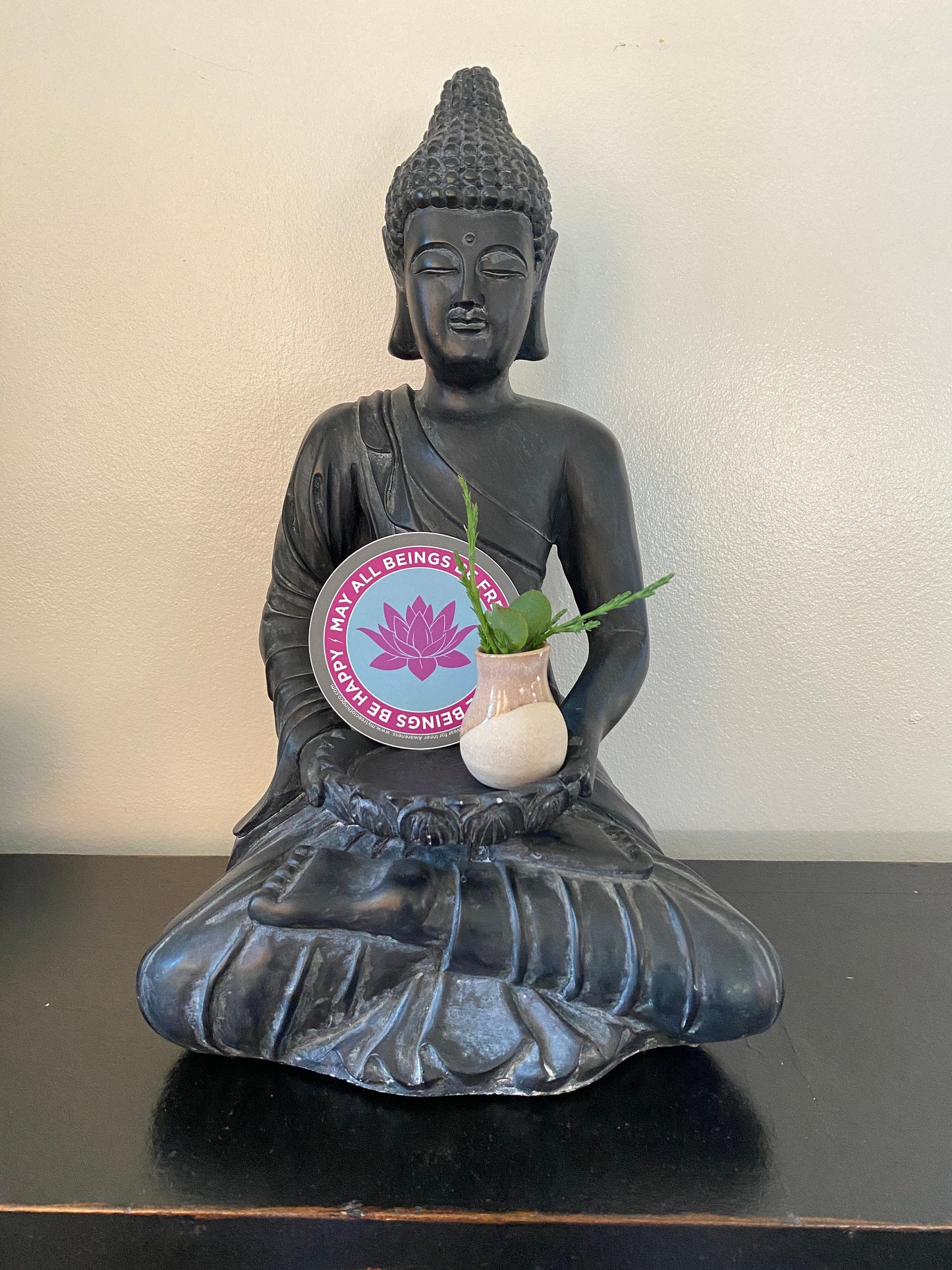 Buddha statue holding a small plant with a 4" circular Buddhist sticker with a purple lotus flower and text, may all beings be free may all beings be happy.