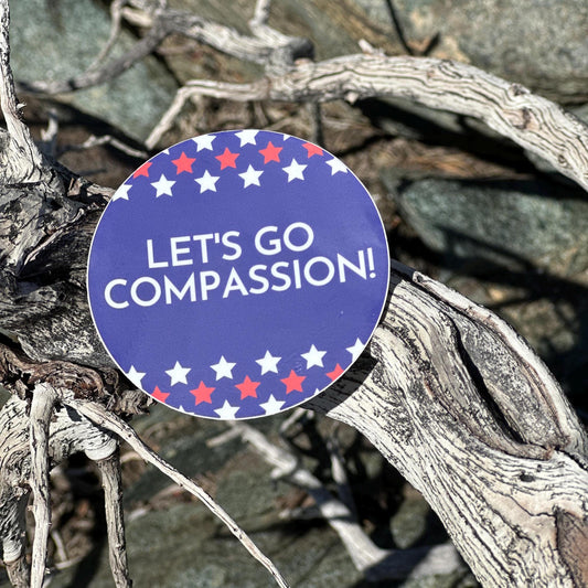 3" round sticker with 'LET'S GO COMPASSION!' text on a natural background.
