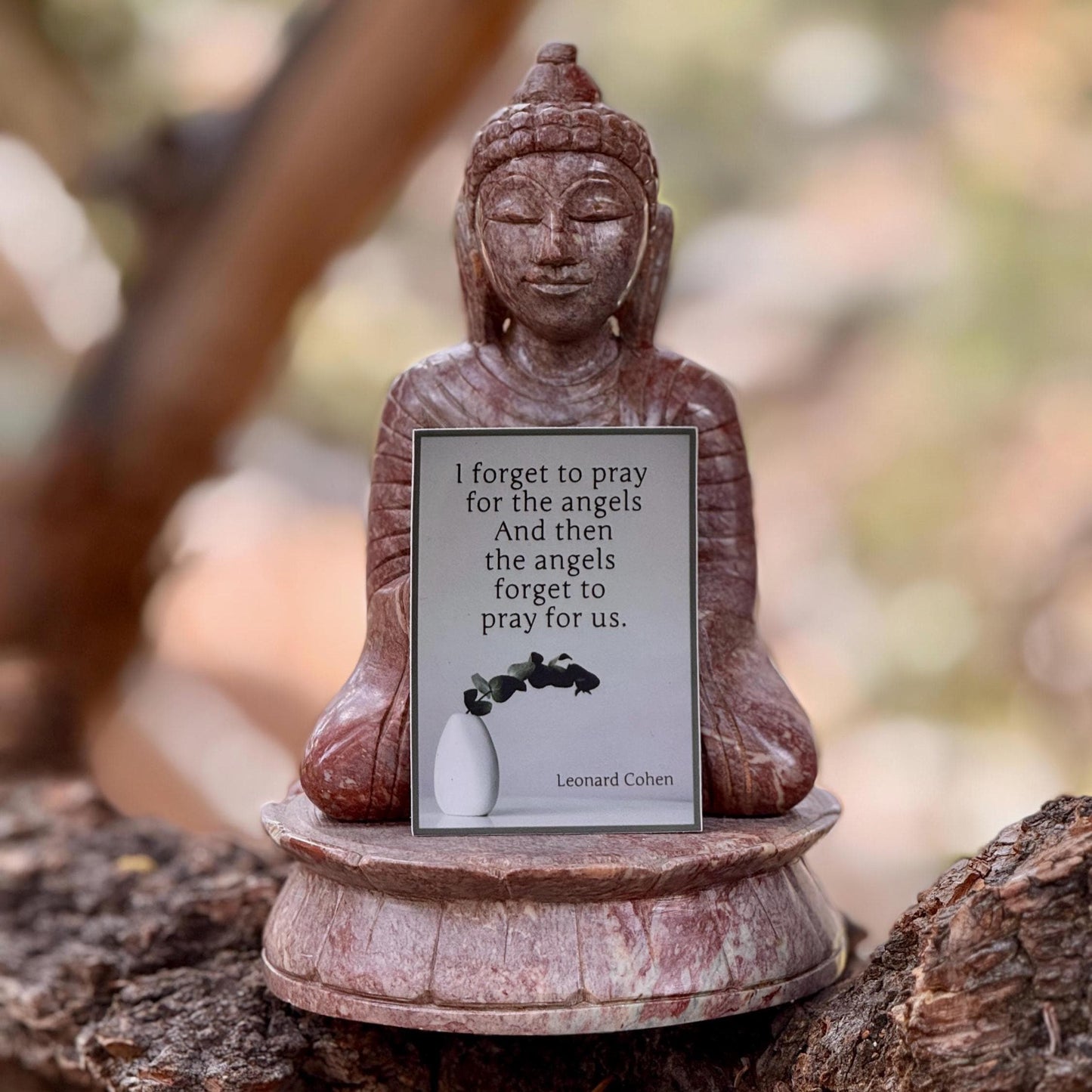 Buddha statue with a Leonard Cohen quote sticker, 'I forget to pray for the angels and then the angels forget to pray for us.'