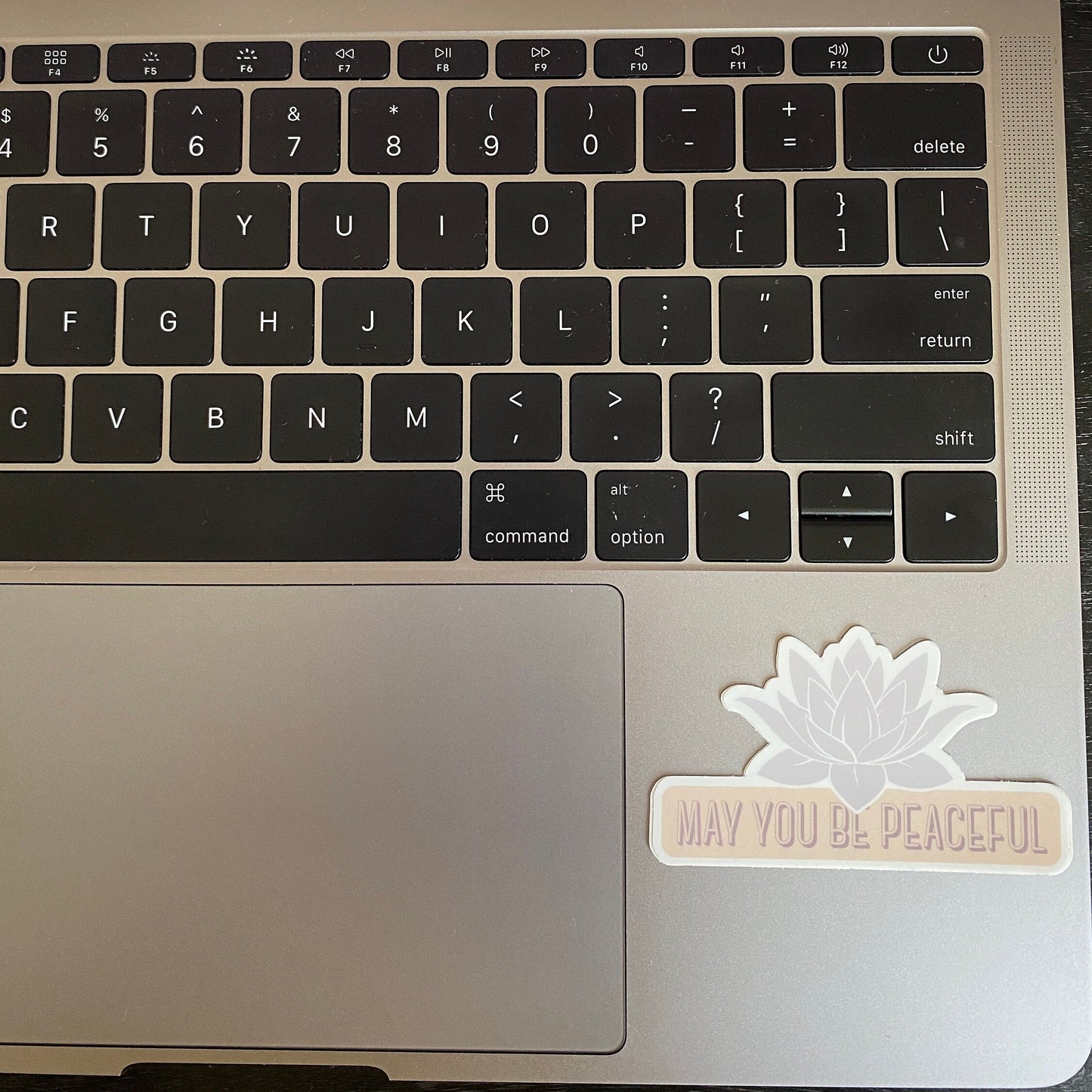 Laptop keyboard with a decorative pale lavender lotus design die cut vinyl sticker with the text, may you be peaceful, on the palm rest area.