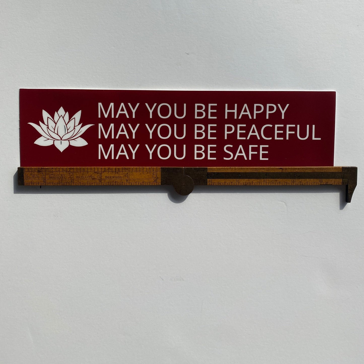 Red and white bumper sticker with a lotus and the prayer, may you be happy may you be peaceful may you be safe.