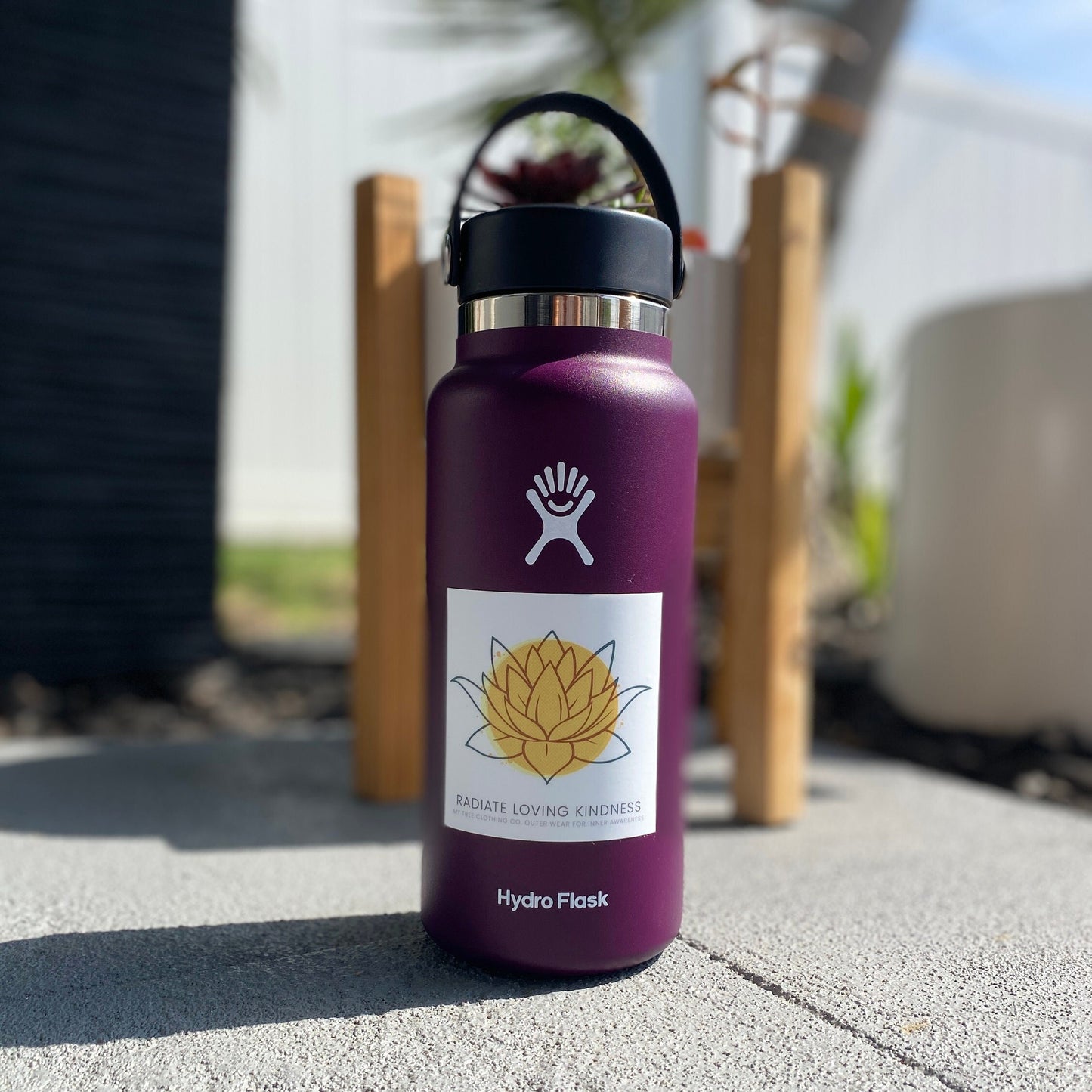 Purple Hydro Flask water bottle with a 'Radiate Loving Kindness' 3" square sticker on a concrete surface