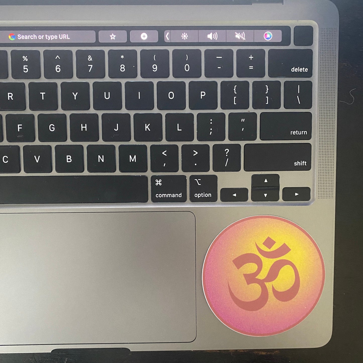 Laptop with a 3" sticker featuring an Om symbol on the palm rest area.