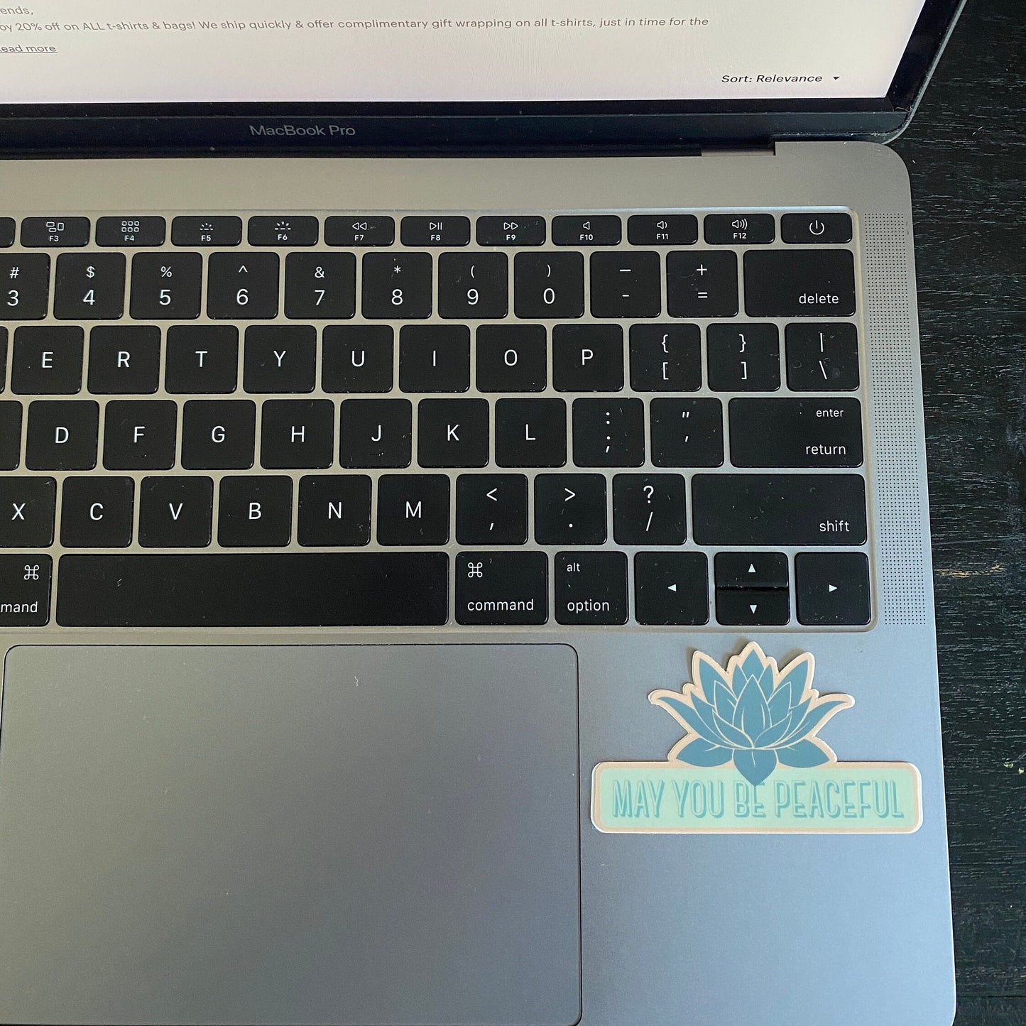 Laptop with a sticker on the palm rest area displaying 'May You Be Peaceful'.