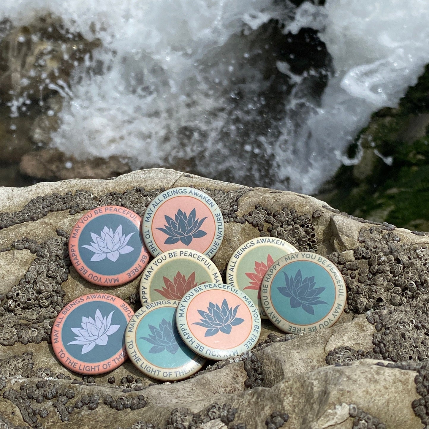 Colorful lotus flower pin back buttons on a rock with water in the background.
