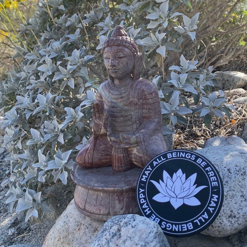 Stone Buddha statue with a 3.5" round black and white magnet with lotus flower design and text, may all beings be free, may all beings be happy' in a natural setting.