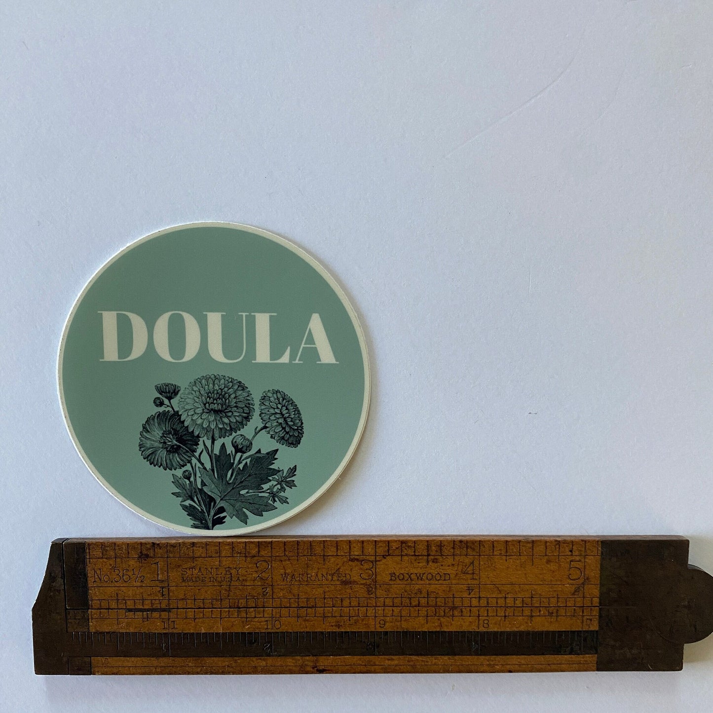 Green coaster with 'DOULA' text and floral design on a white surface with a ruler for scale.
