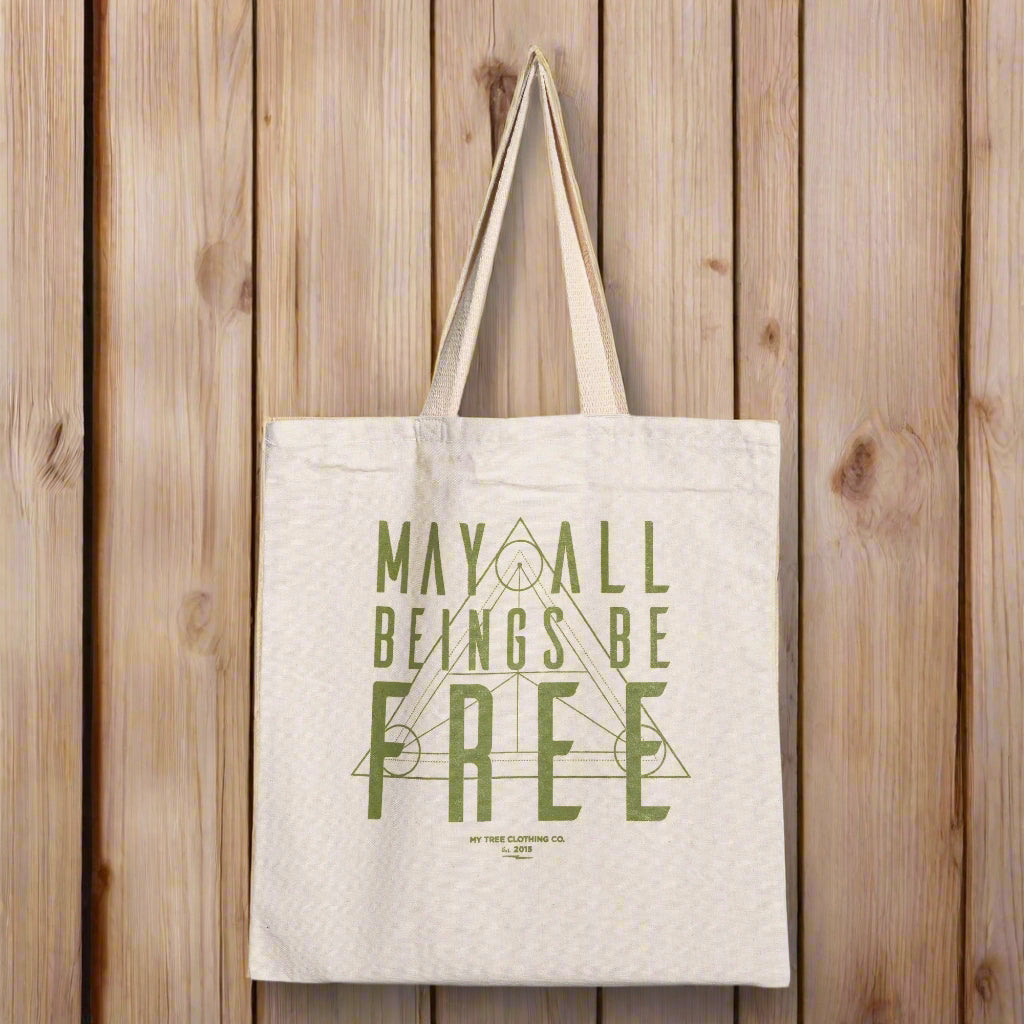 Beige yoga tote bag with green text, may all beings be free, with sacred geometry design.