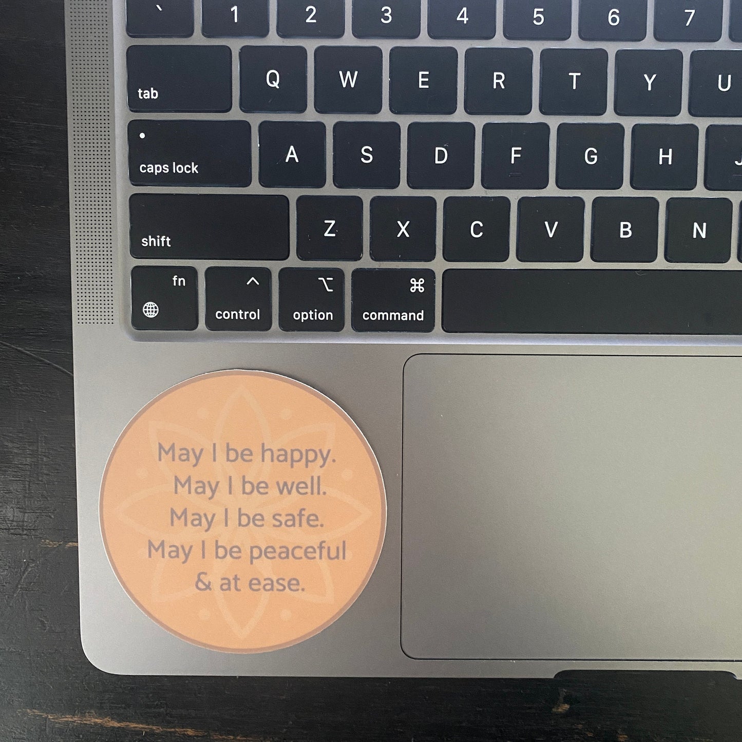 circular sticker with text, may i be happy may i be well may i be safe may i be peaceful may i be at ease. It is attached to a laptop.