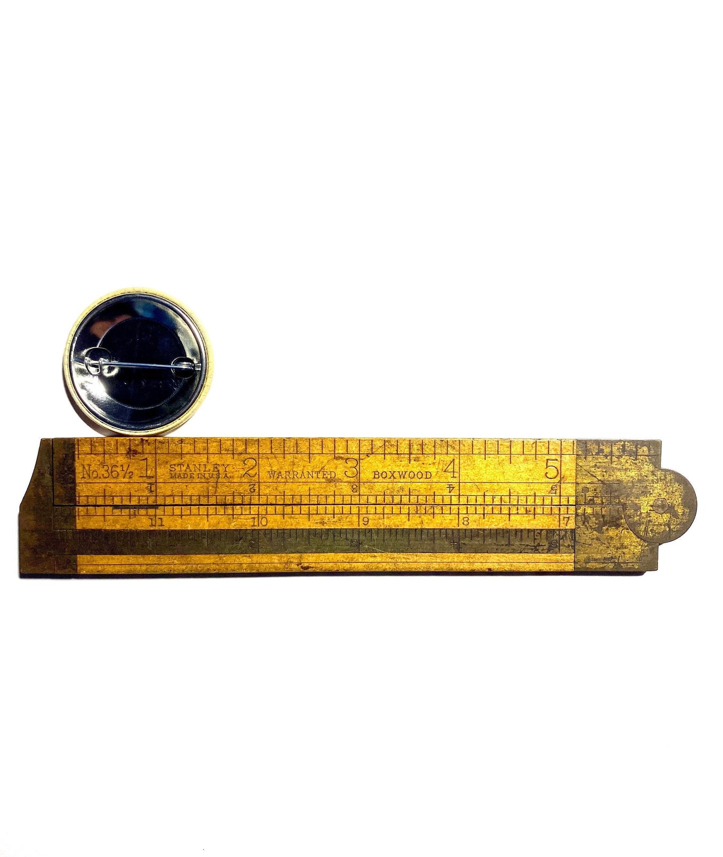 Wooden ruler with a round pin back button on a white background to show scale.