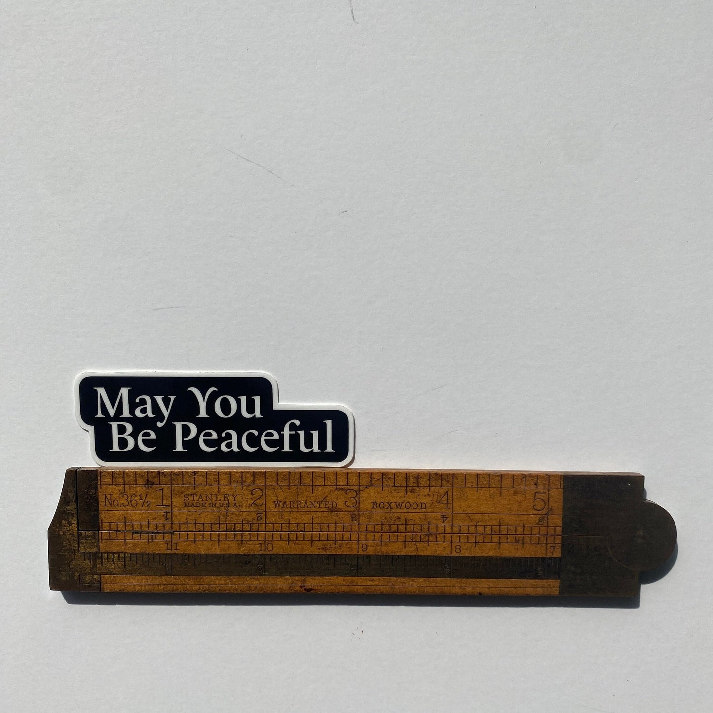 Wooden ruler with 'May You Be Peaceful' text on a white background