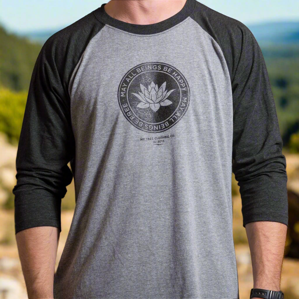 Person wearing a Gray and black 1/4 length sleeve shirt with a lotus logo, and the text, may all beings be free may all beings be happy.