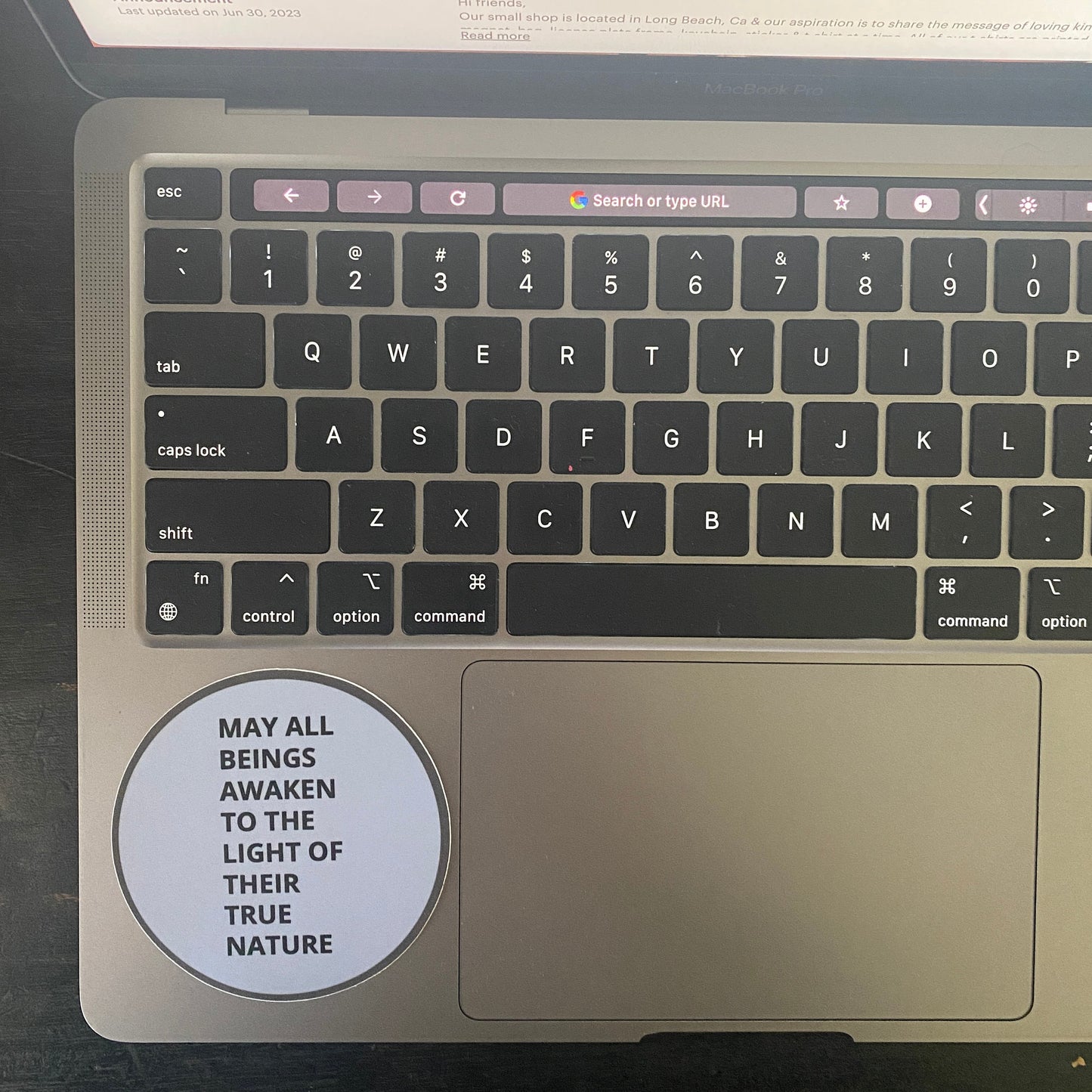 Laptop keyboard with a circular sticker with the text, may all beings awaken to the light of their true nature, on a dark surface.