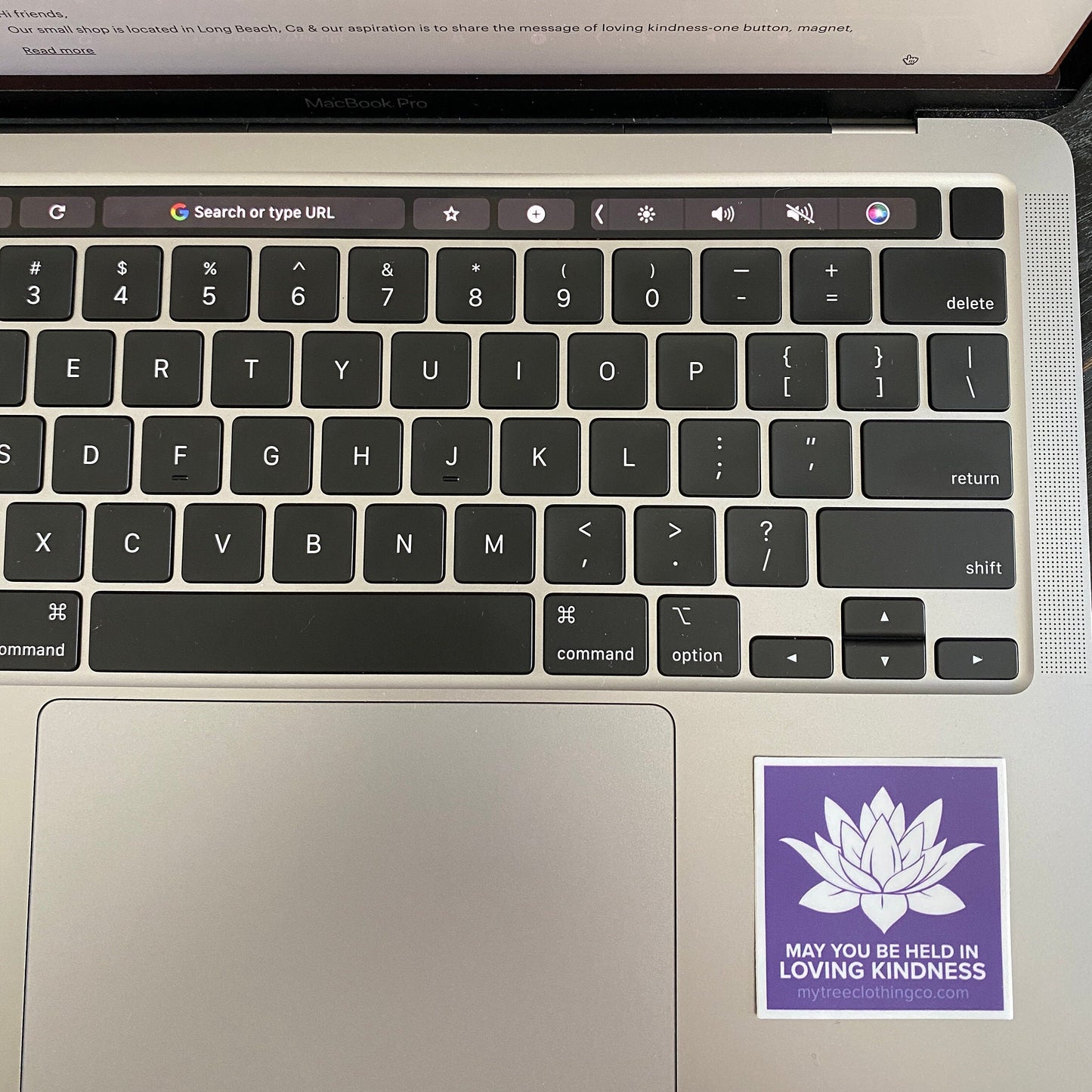 Laptop keyboard with a sticker 2" square purple and white lotus sticker with the words, may you be held in loving kindness. on the palm rest area.