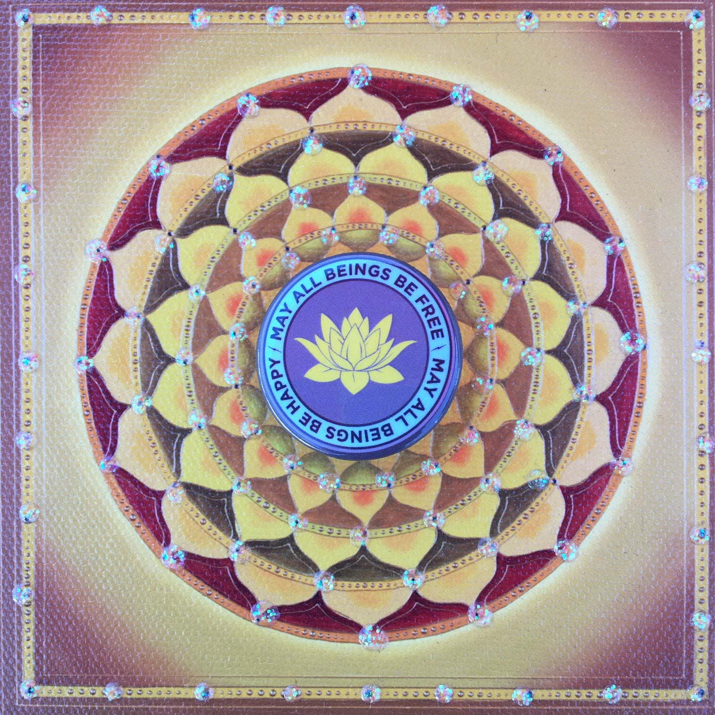 Mandala design with a central lotus symbol and 'May all beings be free may all beings be happy" text on a gold background.