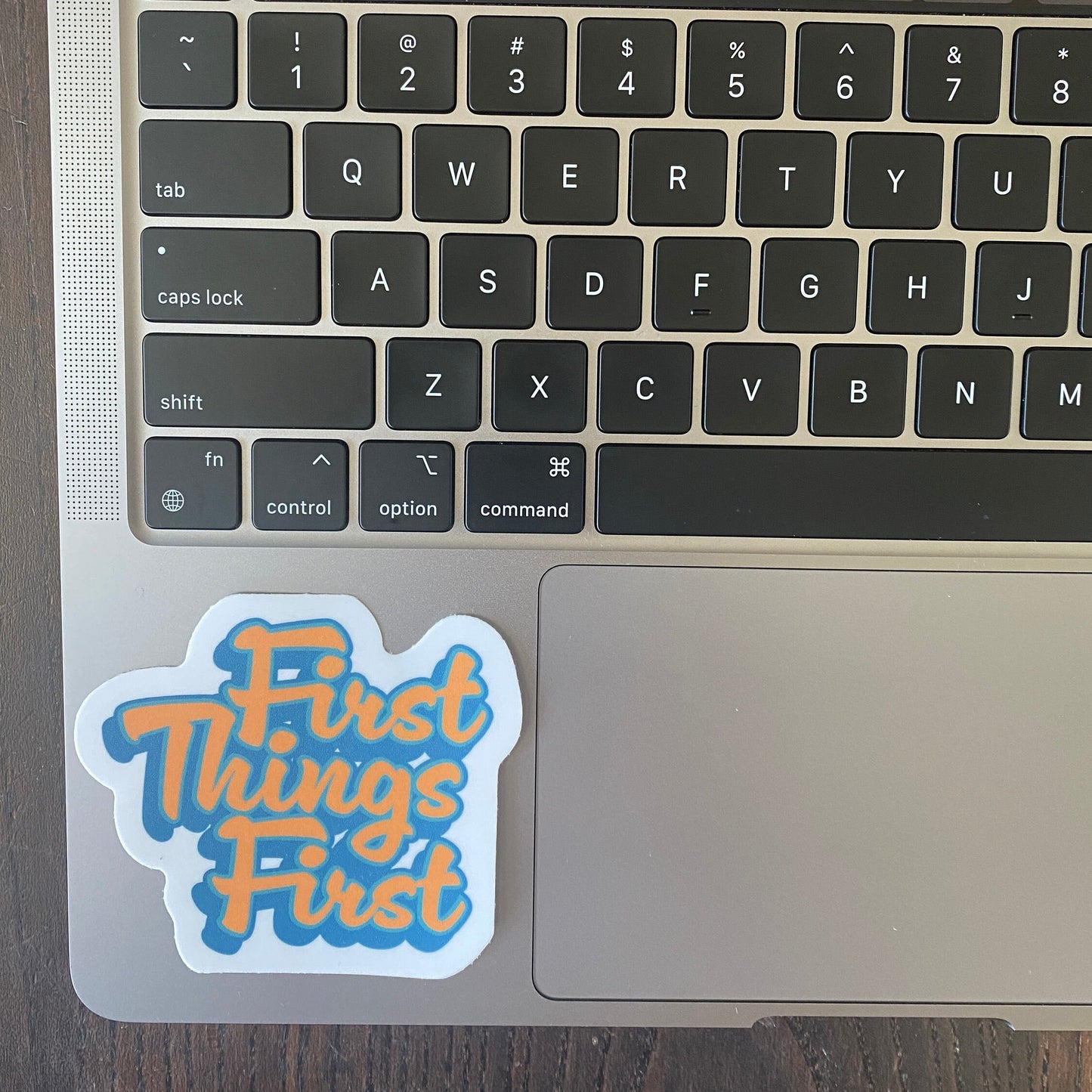 Laptop keyboard with a 'First Things First' sticker on the palm rest area.