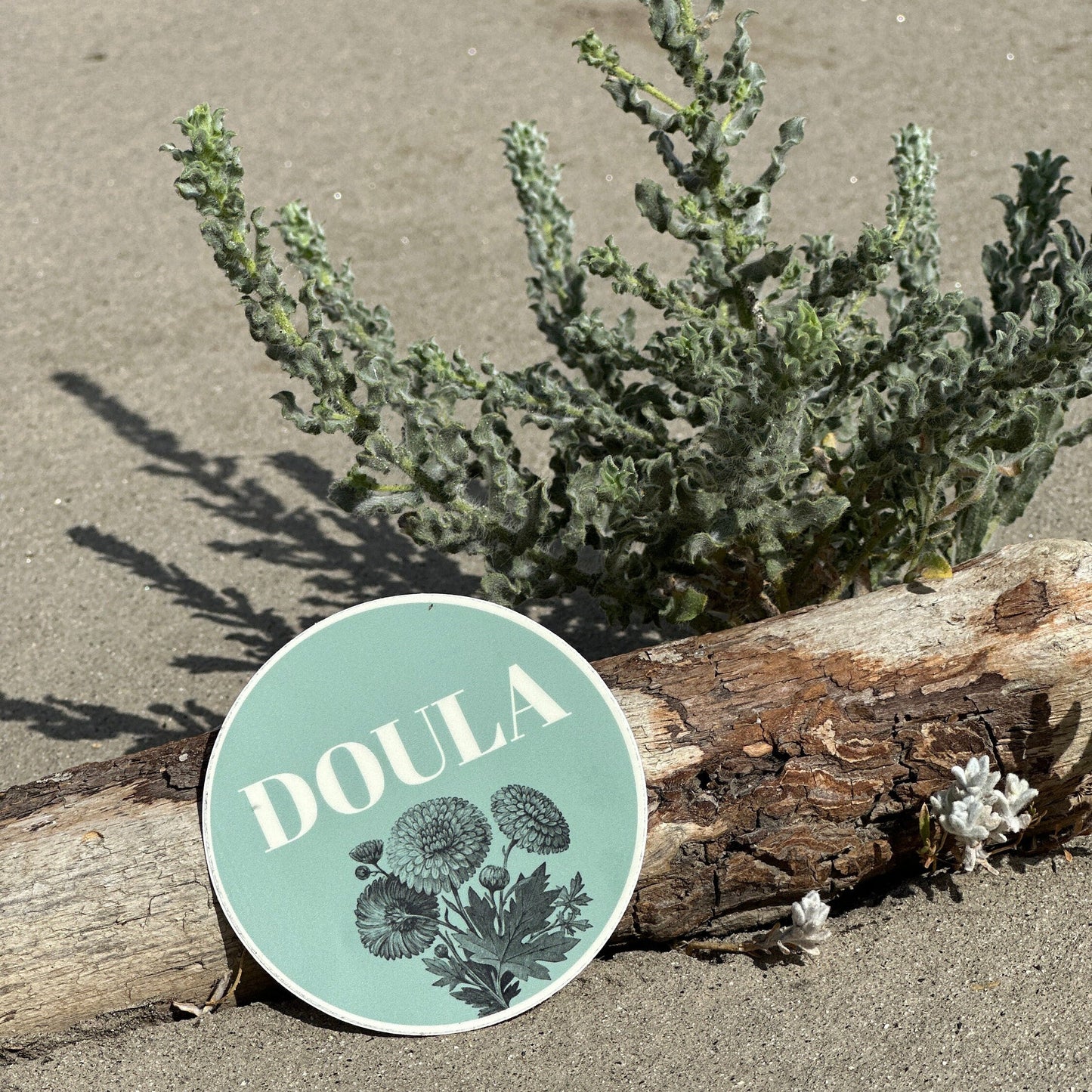 Round 'DOULA' sign with floral design on a sandy background.