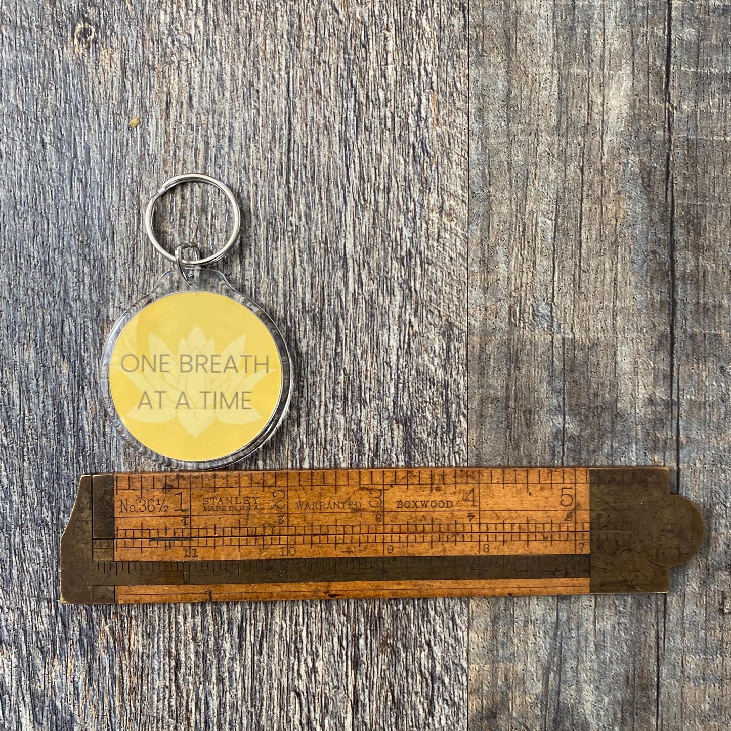2" yellow lotus keychain with 'One Breath at a Time.'