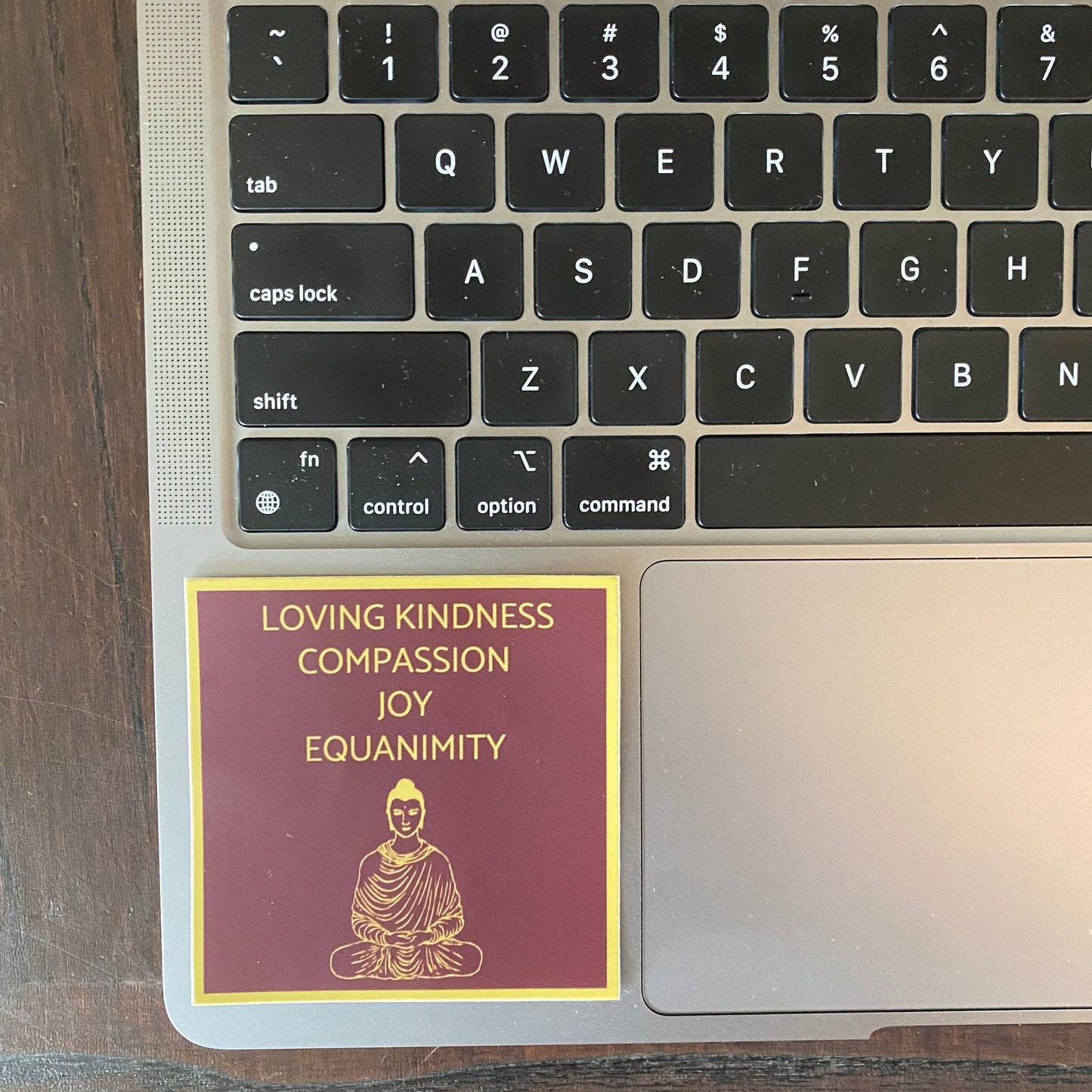 Laptop keyboard with a sticker featuring 'Loving Kindness, Compassion, Joy, Equanimity' and a Buddha illustration.