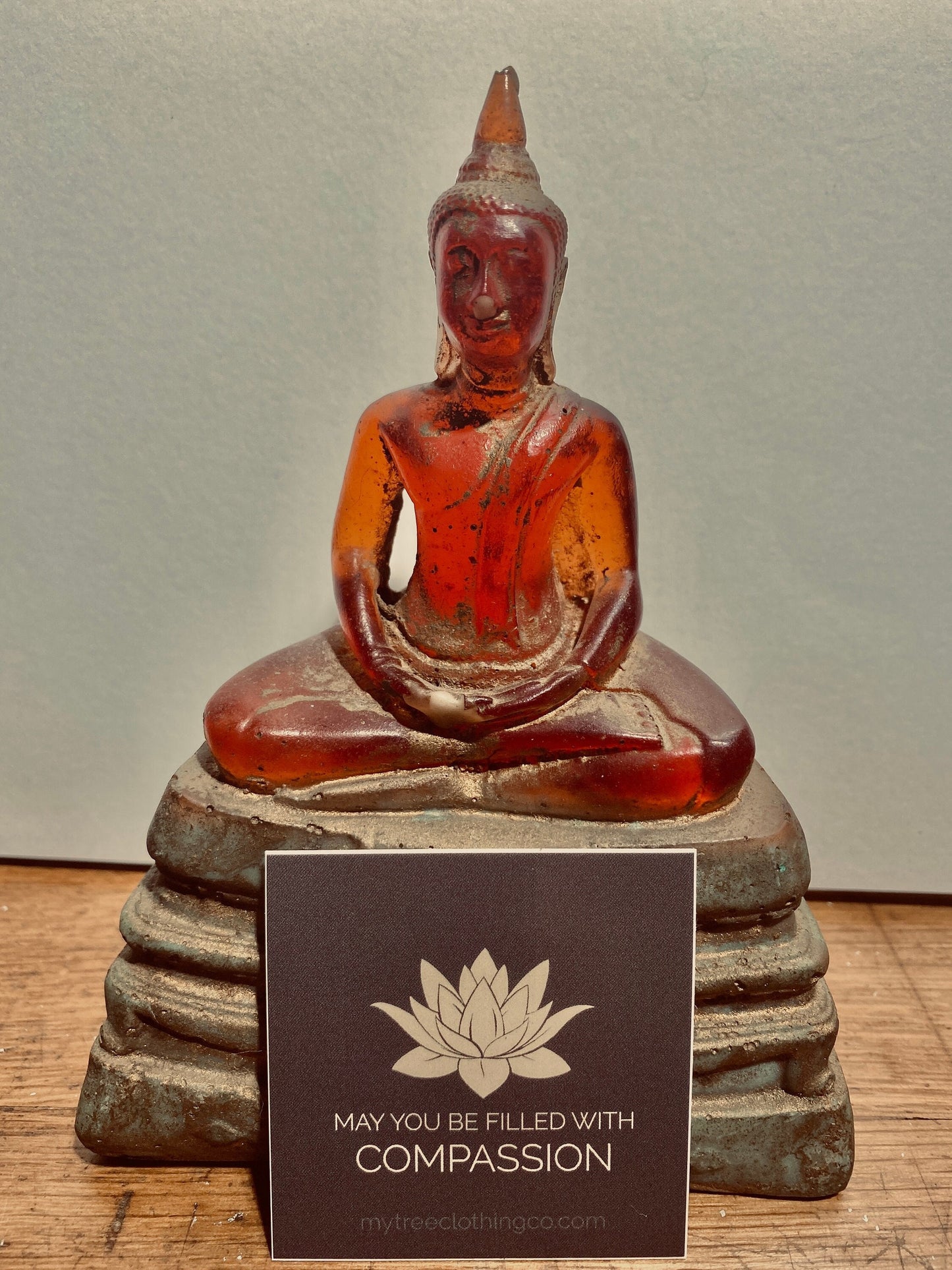 Amber-colored Buddha statue on a stone base with a 2" square lotus flower sticker with text 'May you be filled with compassion.'