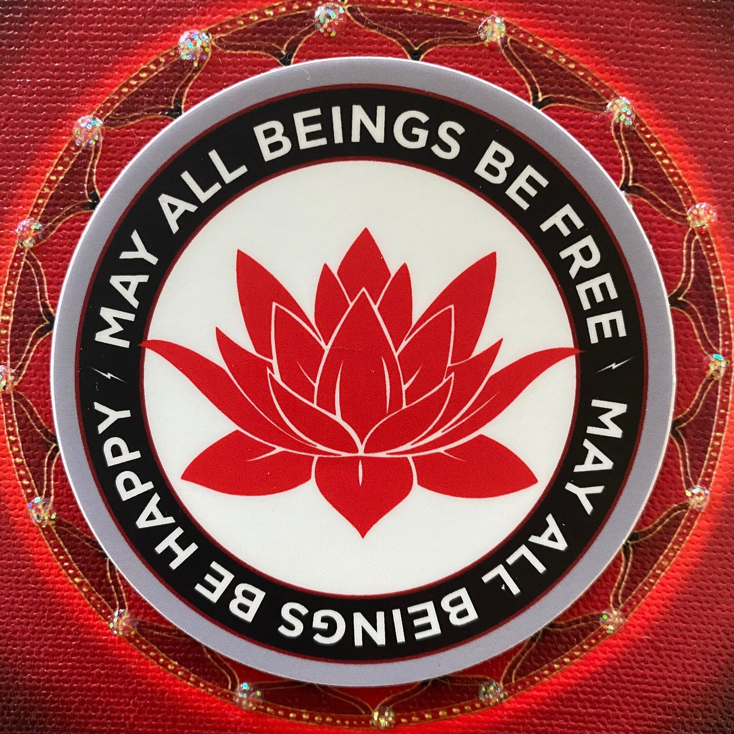 Circular emblem with red lotus flower and text 'May all beings be free, happy' on a red background