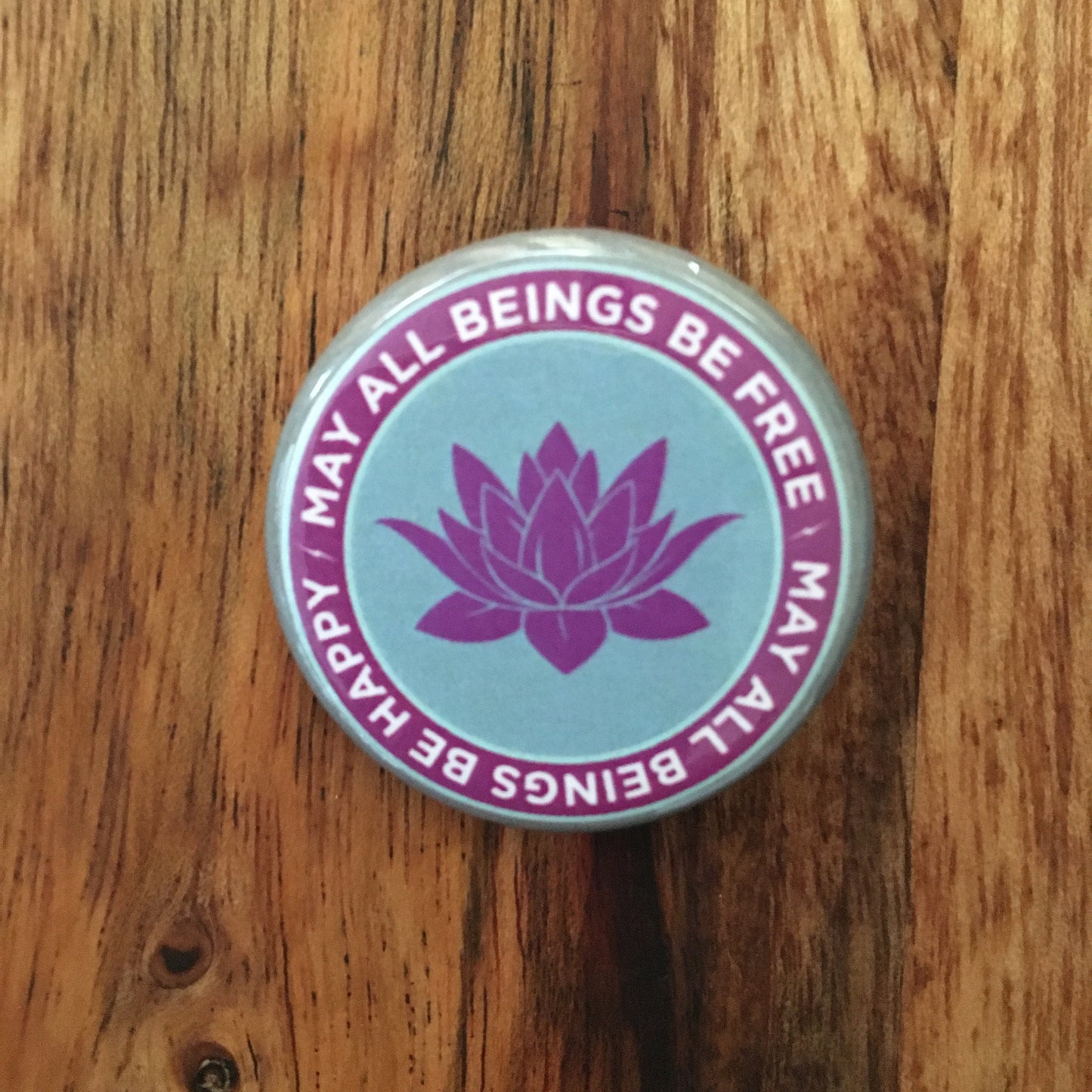 Button badge with lotus flower and text 'May all beings be free' on a wooden surface