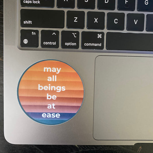 Laptop with a sticker on the palm rest area displaying 'may all beings be at ease'.