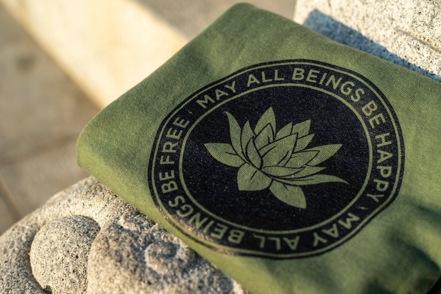 Close up photo of green Buddhist lotus shirt with the text, May All Beings Be Happy May All Beings Be Free.