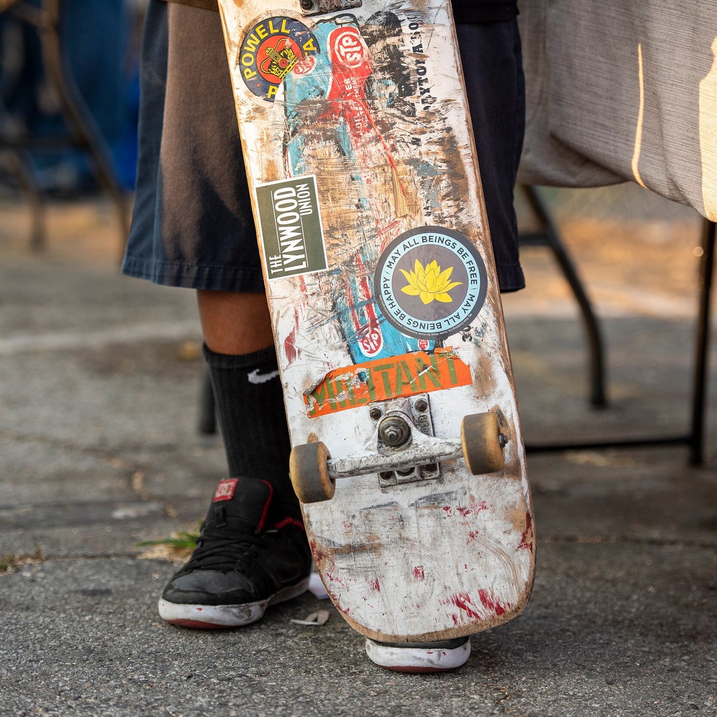Skateboard with stickers held by a person on a concrete surface.