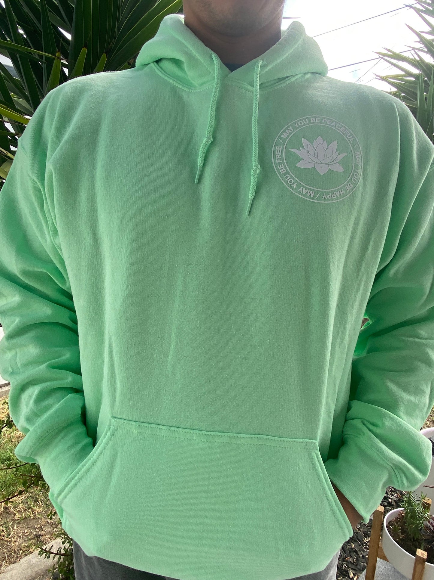 Person wearing a light green hoodie with a lotus, standing outdoors.