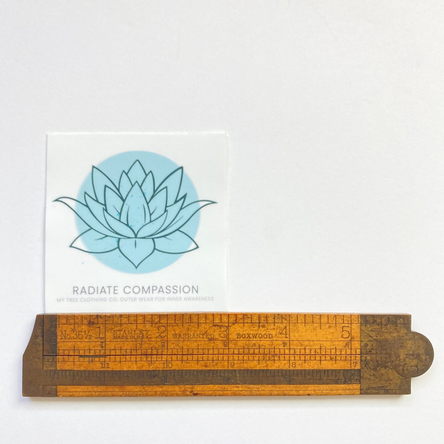 Wooden ruler with a 3" square sticker with a blue lotus design and text, radiate compassion.