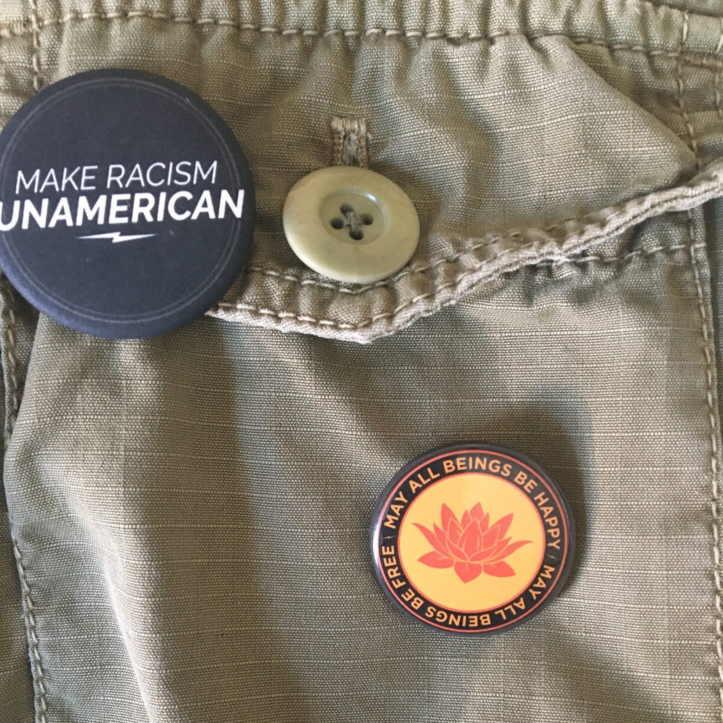 Button with 'Make Racism Unamerican' text on a jacket with another button and a 1.25" Orange round pin back button with a buddhist lotus flower and the text 'may all beings be happy may all beings be free.'