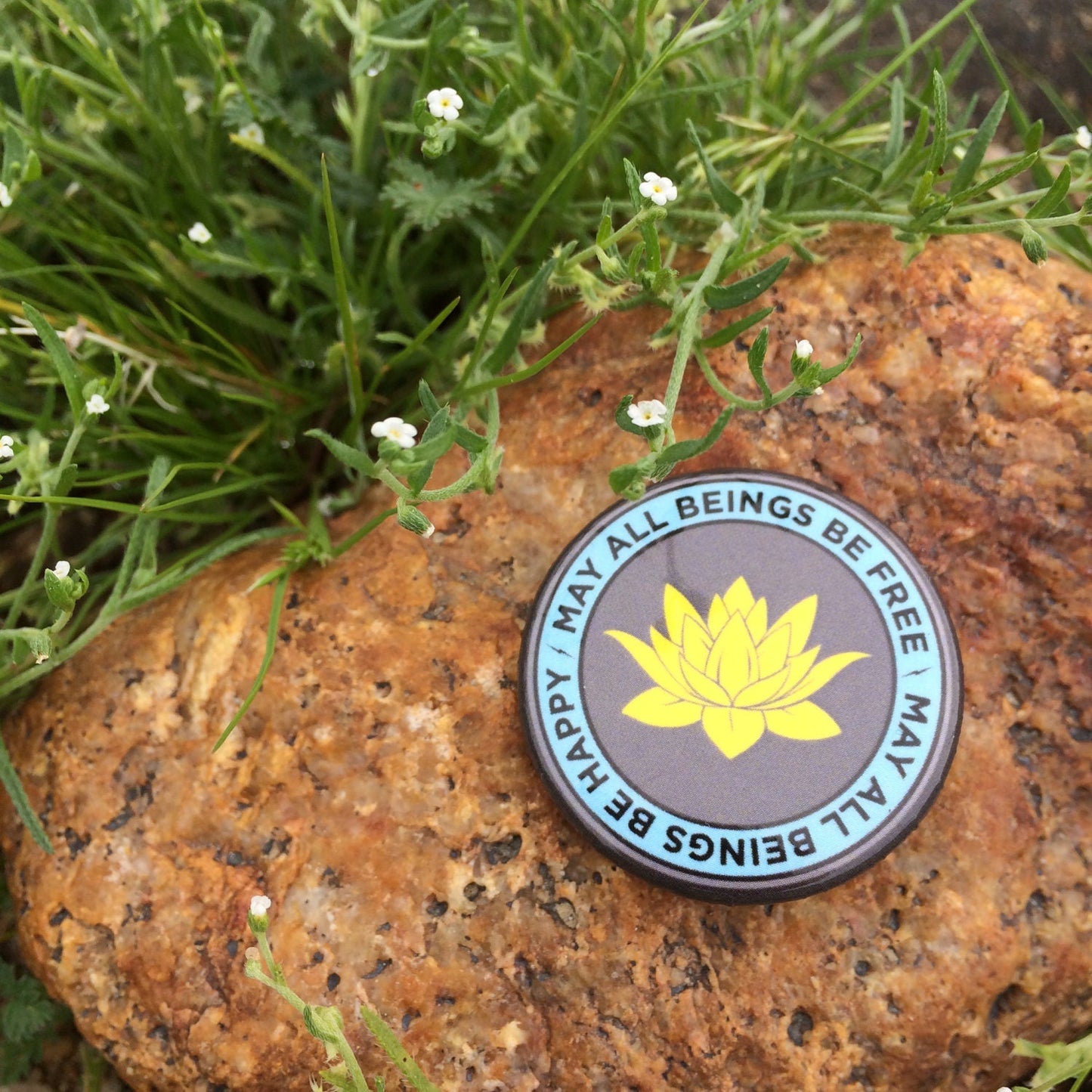 Round badge with a yellow lotus flower design on a rock surrounded by greenery