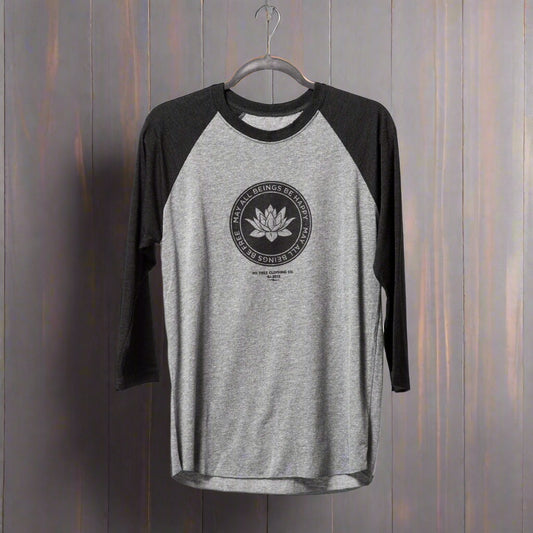 Gray and black 1/4 length sleeve shirt with a lotus logo, and the text, may all beings be free may all beings be happy. Hanging on a hanger with a wooden background.